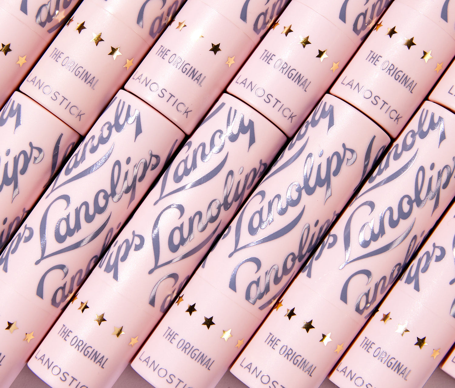A close up of multiple Lanolips Lanostick tubes arranged in a diagonal pattern. This 90s-inspired wind-up lip balm is perfect for on-the-go hydration, fitting easily into pockets and bags. From the makers of the 'World’s Best Lip Balm,' Lanostick glides on smoothly, delivering a rich layer of moisture that deeply conditions lips. Formulated with lanolin, natural waxes, butters, and vitamin E, it nourishes and locks in hydration for hours. The ultimate day-balm for soft, healthy lips.