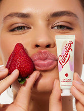 Load image into Gallery viewer, Model holding Lanolips Lip Scrub Strawberry and with the mixture of ultra-pure grade lanolin, finely ground strawberry seeds and sugar, it leaves your lips deeply hydrated.
