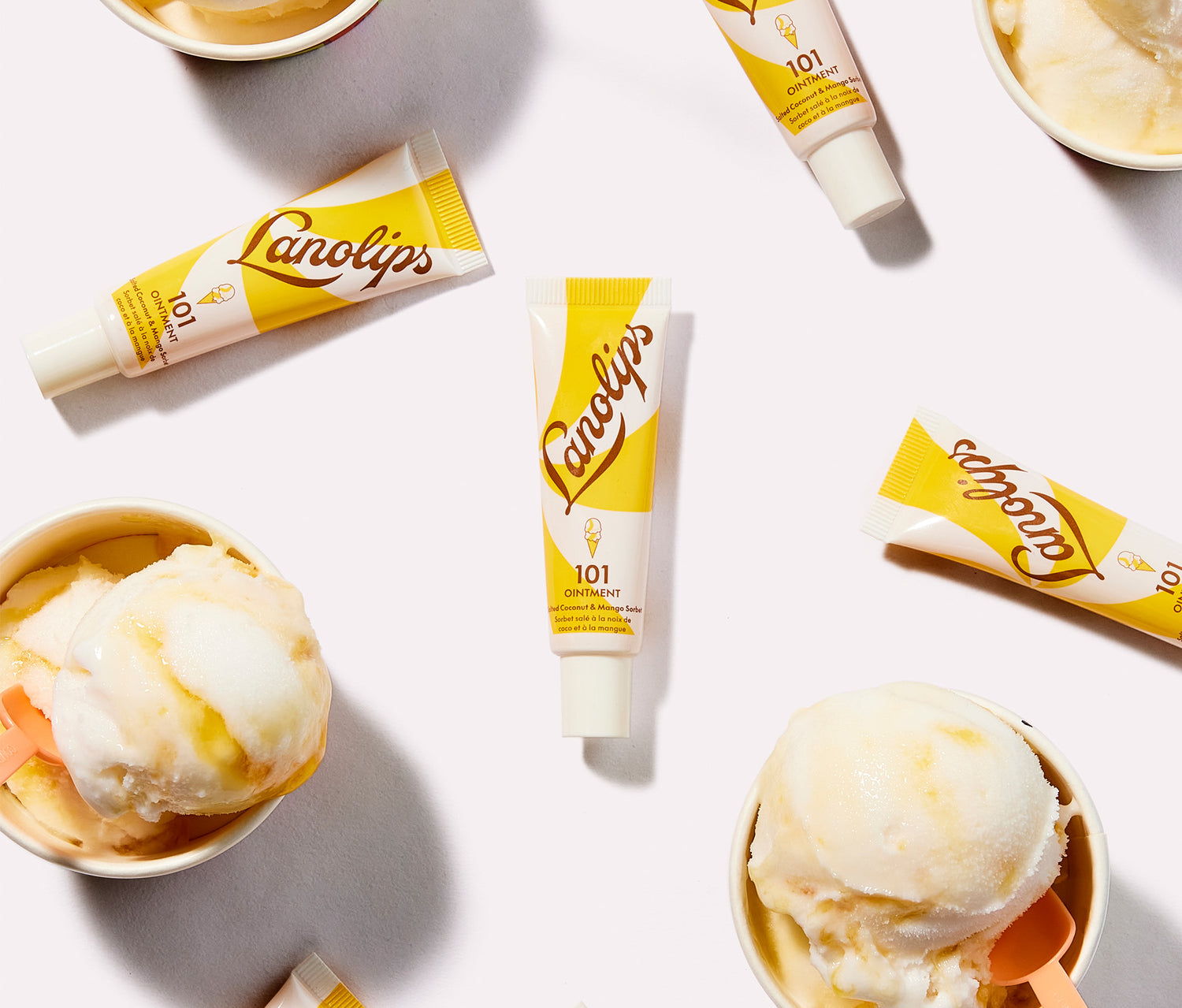 Lanolips x MESSINA 101 Ointment Multi Balm in Salted Coconut & Mango Sorbet, surrounded by  scoops of creamy mango and coconut sorbet in small cups. The balm's yellow and white packaging complements the dessert-inspired theme. Made with lanolin, vitamin e and natural coconut oil and mango fruit extract, for a naturally sweet hydration boost throughout the day. The super rich balm gives long lasting hydration for dry and chapped lips, skin patches, cuticles, elbows and more. 