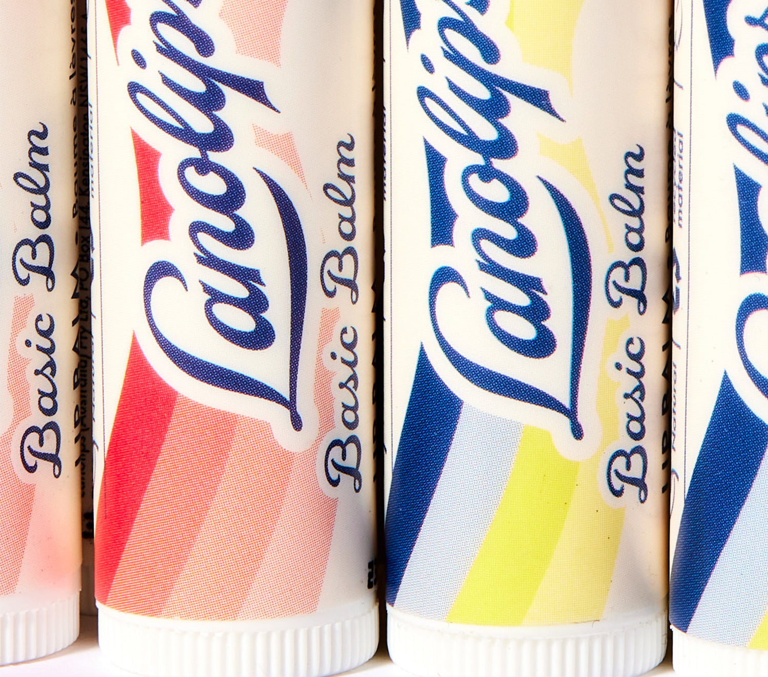 Close-up of Lanolips Basic Balm tubes in fruity flavours: Original Vanilla, Strawberry, and Coconutter. Made with 100% natural lanolin, shea butter, jojoba, and vitamin E, this ultra-hydrating balm keeps lips soft and nourished. Simple, sustainable lip care in a low-fi wind-up stick.
