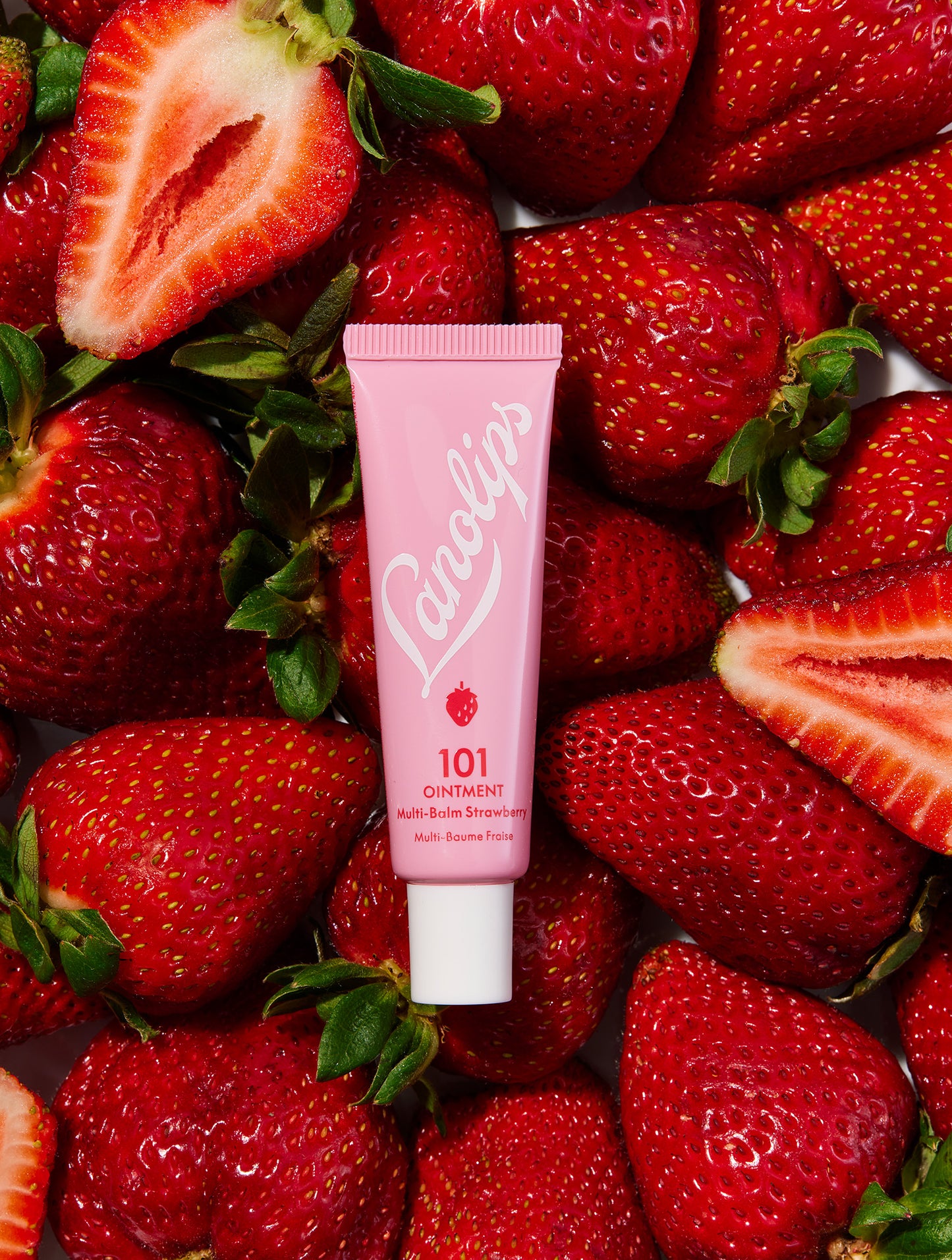 Flat lay of a tube of Lanolips 101 Ointment Multi-Balm in Strawberry laid with fresh strawberries. Made with ultra-pure grade lanolin, and infused vitamin e and natural strawberry flavours for a fruity twist.