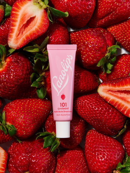Flat lay of a tube of Lanolips 101 Ointment Multi-Balm in Strawberry laid with fresh strawberries. Made with ultra-pure grade lanolin, and infused vitamin e and natural strawberry flavours for a fruity twist.