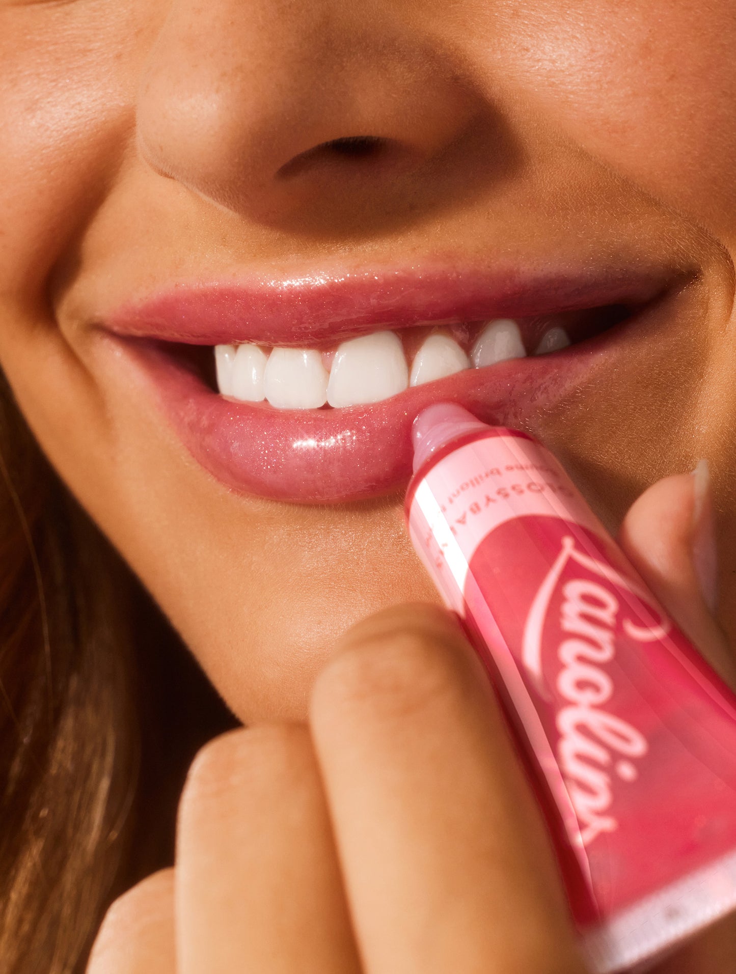 Close up image of a model applying lanolips glossy balms candy lip balm to her lips.