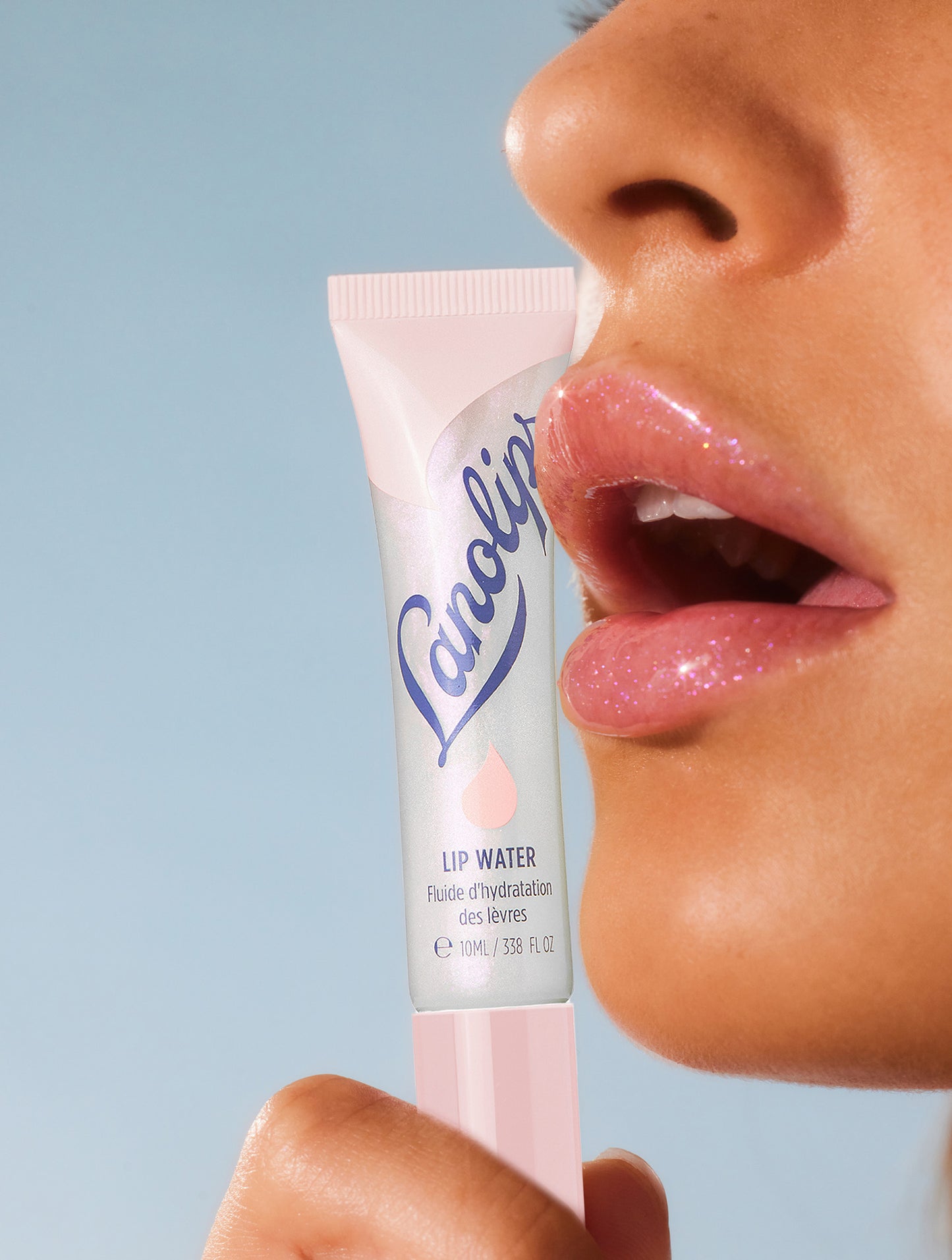 Close up shot of a model holding the Lip Water Original tube against the models lips showing the Lanolips Lip Water Original non sticky, glow finish.