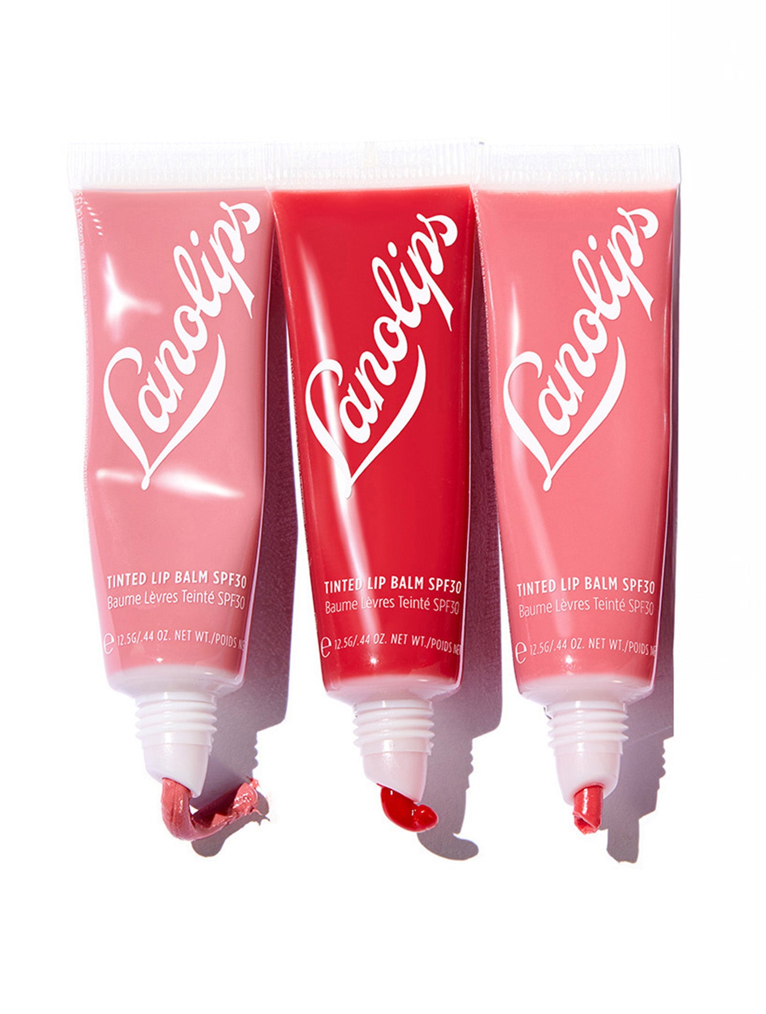 Close-up of the squeezed Lanolips Tinted Lip Balm SPF30 tubes in shades rose, red apple and rhubarb. Formulated with hydrating lanolin, vitamin E, and shea butter for soft, nourished lips. The SPF30 protection helps shield against sun damage while providing a natural, de