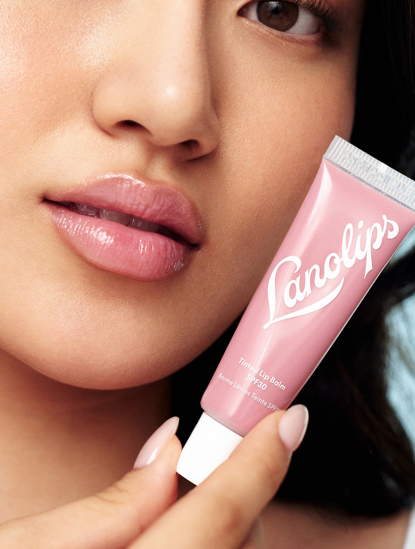 Close up shot of a model wearing a sheer colour tint from a lanolin-rich lip moisturiser with SPF30. She holds a tube of Lanolips Tinted Lip Balm SPF30 in Rose, formulated with hydrating lanolin, vitamin E, and shea butter for soft, nourished lips. The SPF30 protection helps shield against sun damage while providing a natural, dewy finish.