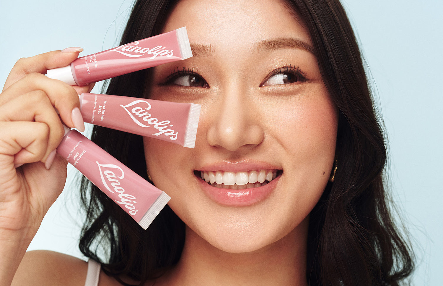 Model holding a lanolips tinted lip balm tubes in her hand.